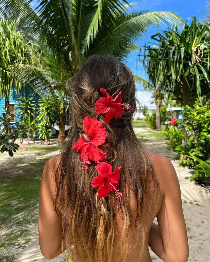 a woman with long hair and red flowers in her hair is standing on the beach