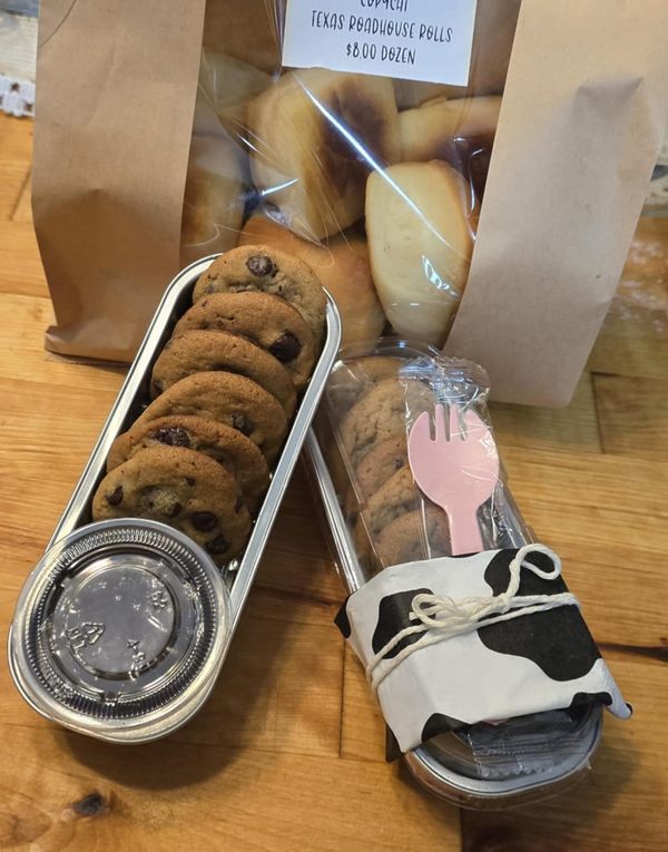 two tins filled with cookies and pastries on top of a wooden table next to brown paper bags