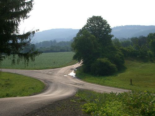 an empty road in the middle of a green field