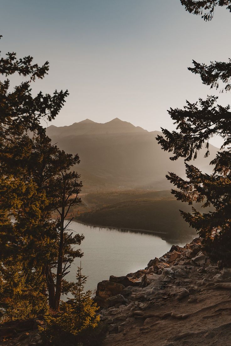 the sun is setting over a lake with mountains in the distance and trees around it