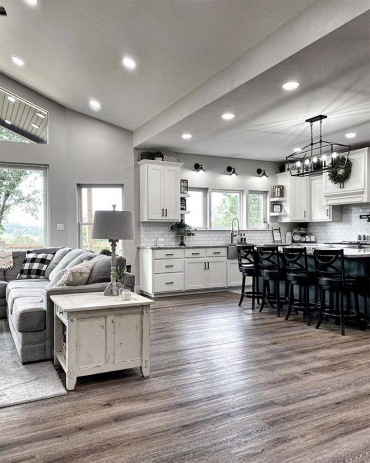 a large open concept kitchen and living room with wood flooring, white cabinets and gray couches