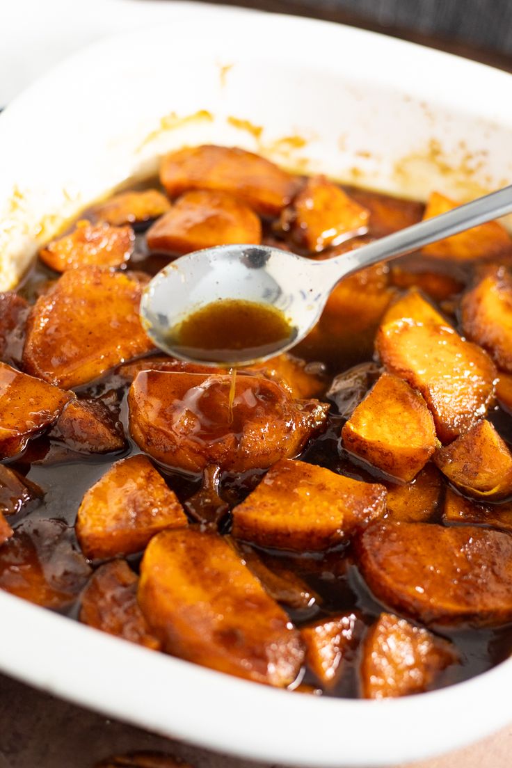 a spoon in a dish full of sweet potatoes with sauce on the side and brown liquid