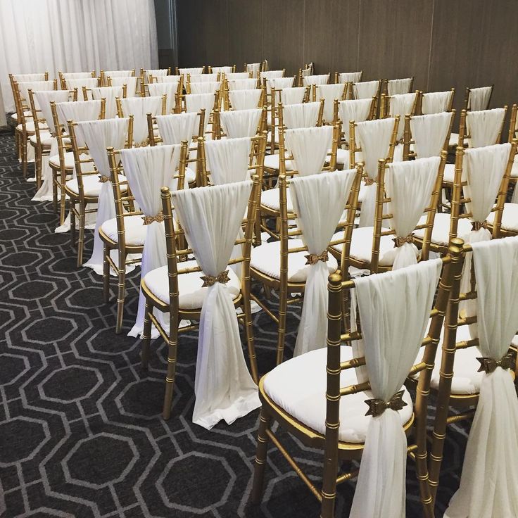 rows of gold chairs with white sashes and bows on them in a conference room