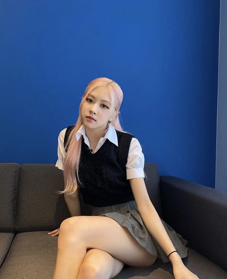 a woman sitting on top of a gray couch next to a blue wall with her legs crossed