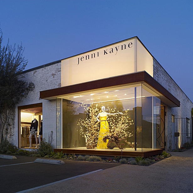 a store front at night with the lights on and people walking in the window area