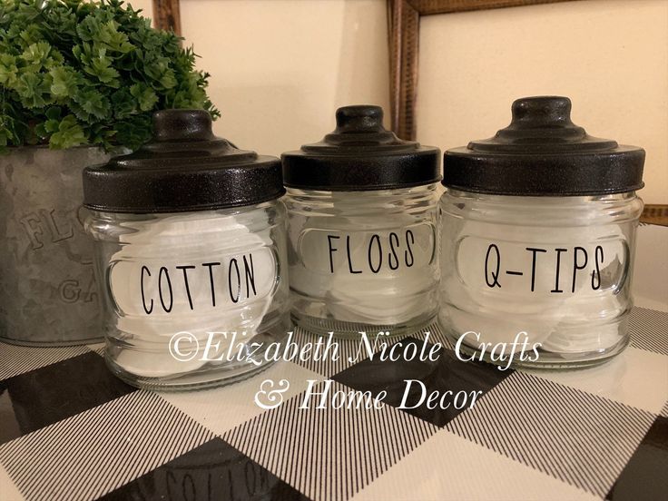 three glass jars with labels on them are sitting on a checkered tablecloth next to a potted plant