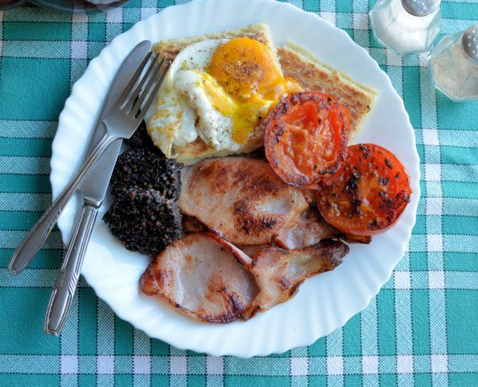 a white plate topped with meat and eggs next to fruit on a blue checkered table cloth