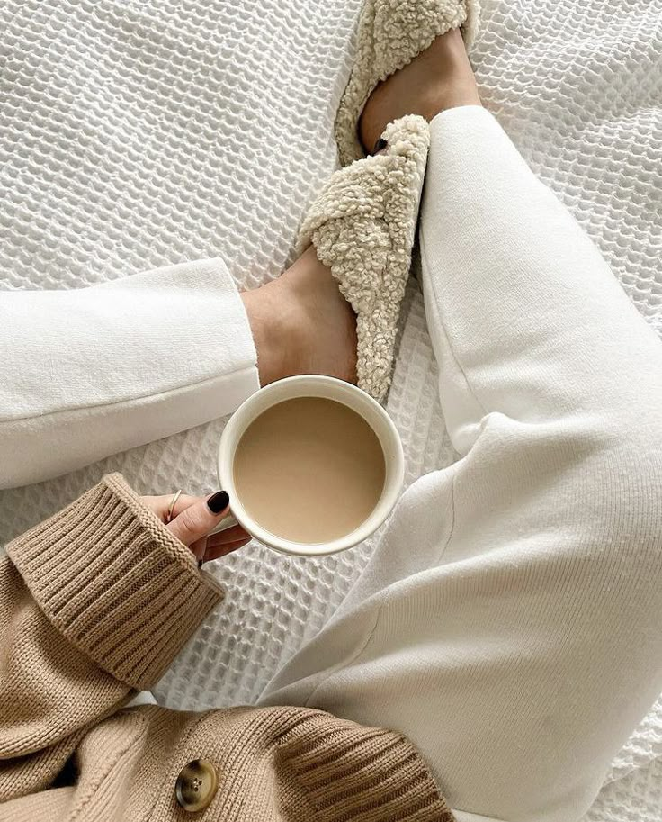 a woman is holding a cup of coffee while laying on the bed with her feet up