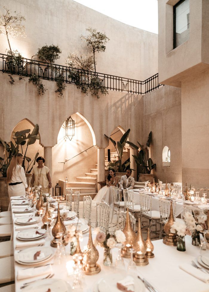 a dining room with tables and chairs covered in white tablecloths, gold plates and silverware