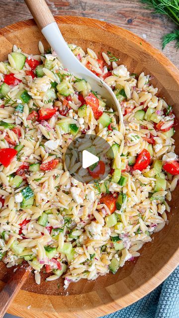 a wooden bowl filled with pasta salad and a serving spoon in the bowl next to it