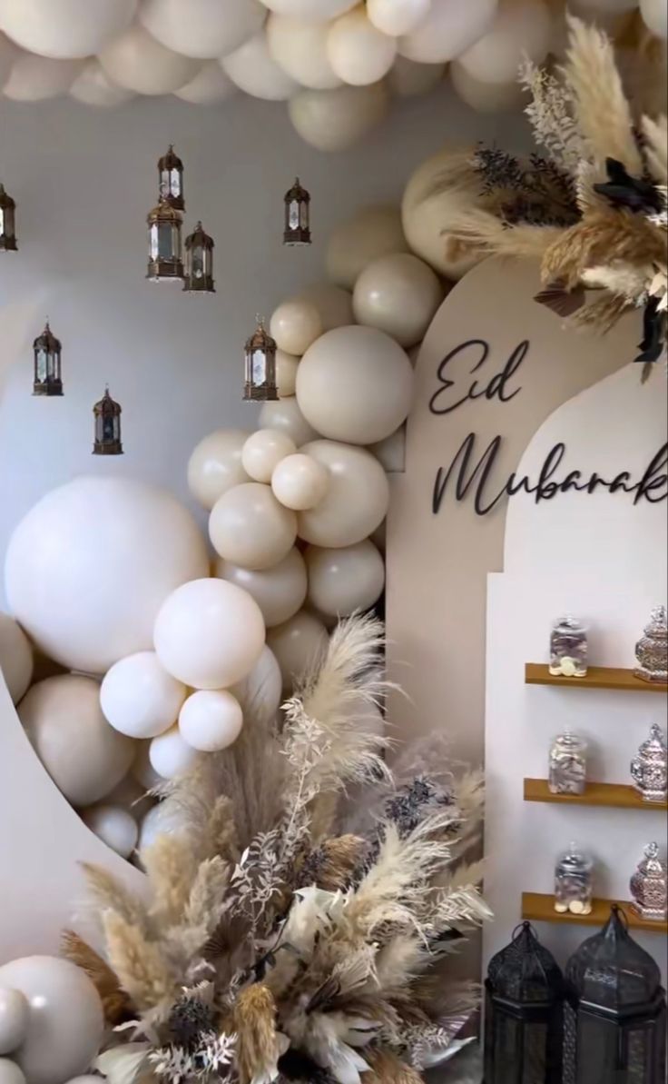 balloons are hanging from the ceiling in front of a wall with white and gold decorations