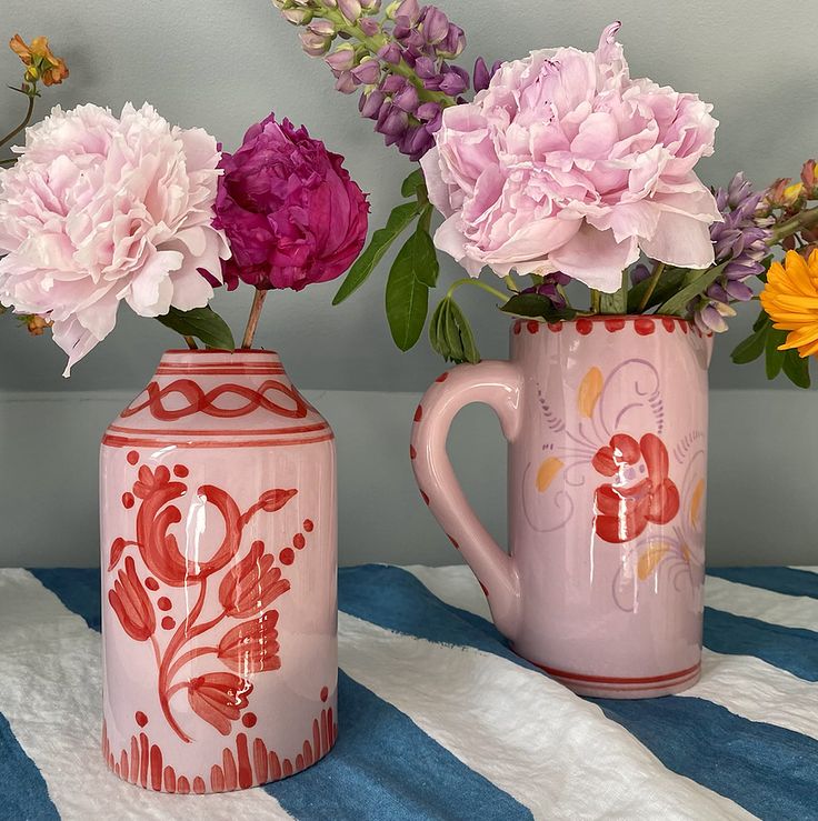 two vases with flowers in them sitting on a striped table cloth next to each other