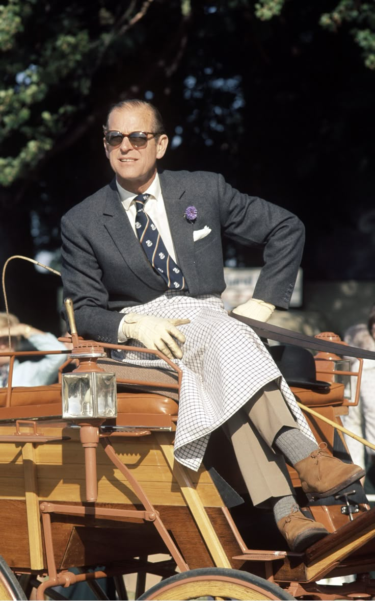 a man in a suit and tie sitting on a horse drawn carriage with people behind him