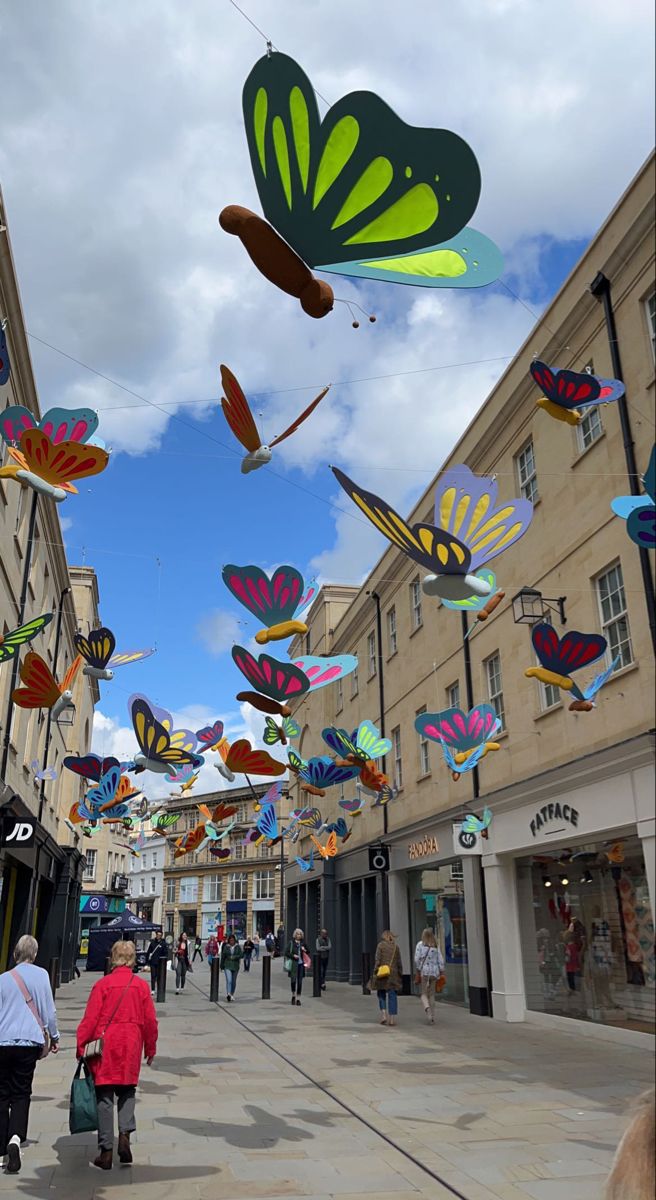 many colorful kites are being flown in the air on a city street as people walk by