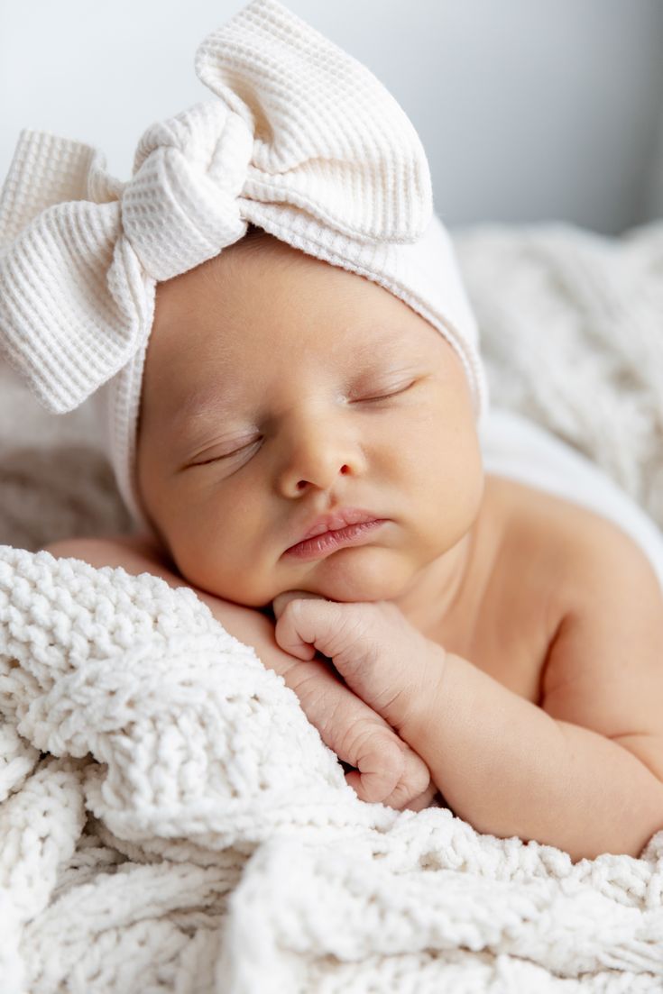 a baby sleeping on top of a blanket wearing a white headband with a big bow