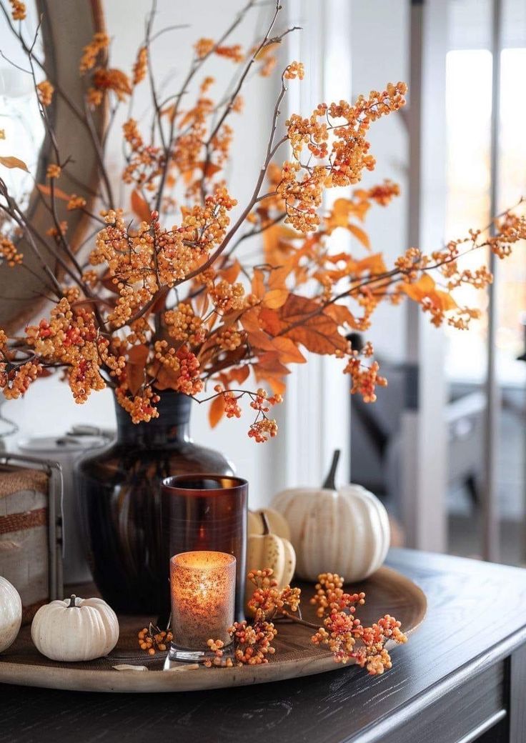 an arrangement of flowers and candles on a table in front of a mirror with pumpkins