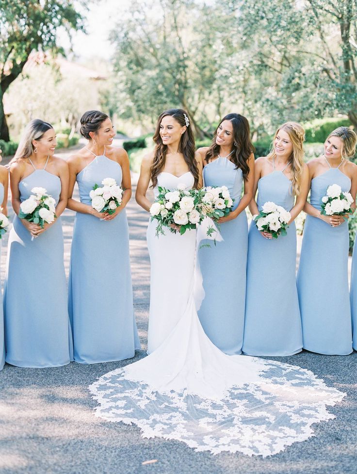 a group of women standing next to each other wearing blue dresses and holding bouquets