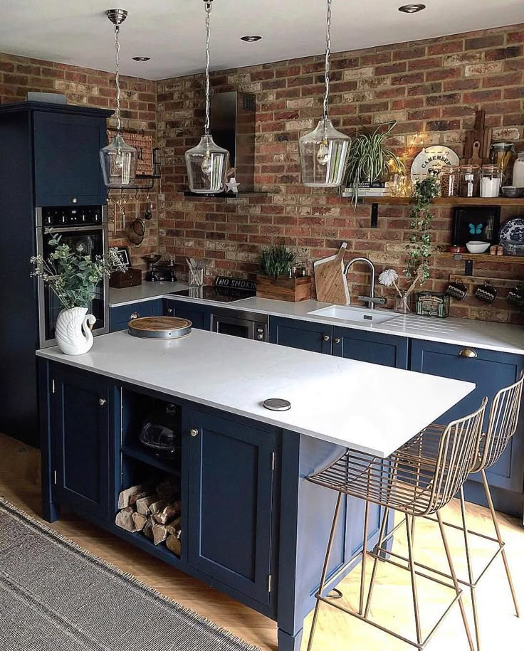 a kitchen with blue cabinets and an island in front of a brick wall that has potted plants on it