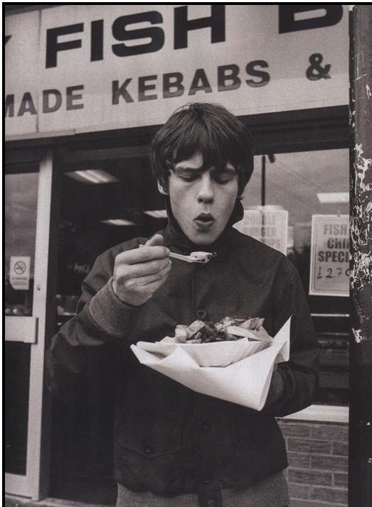 a young man eating food from a paper bag in front of a fish and chip shop