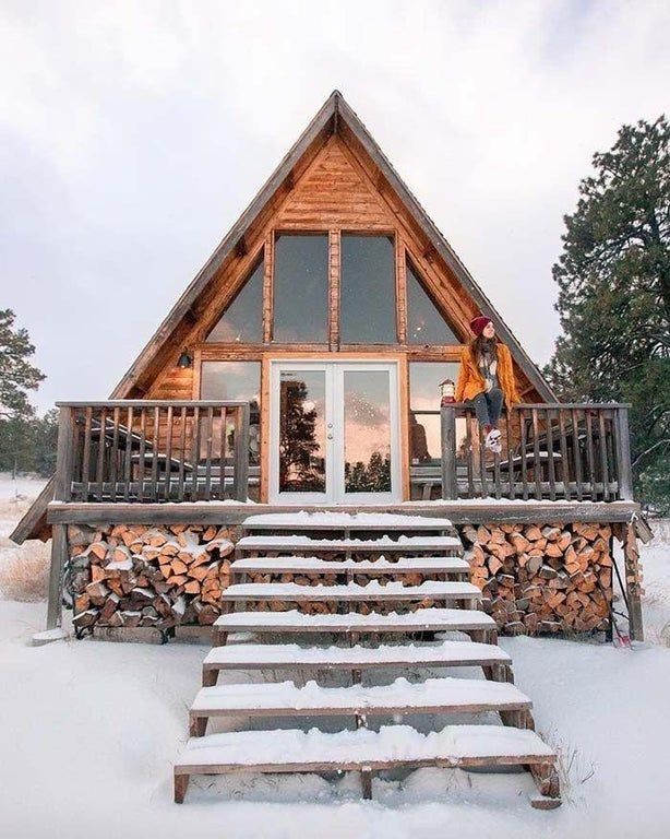 a person standing on the porch of a cabin in the snow with stairs leading up to it