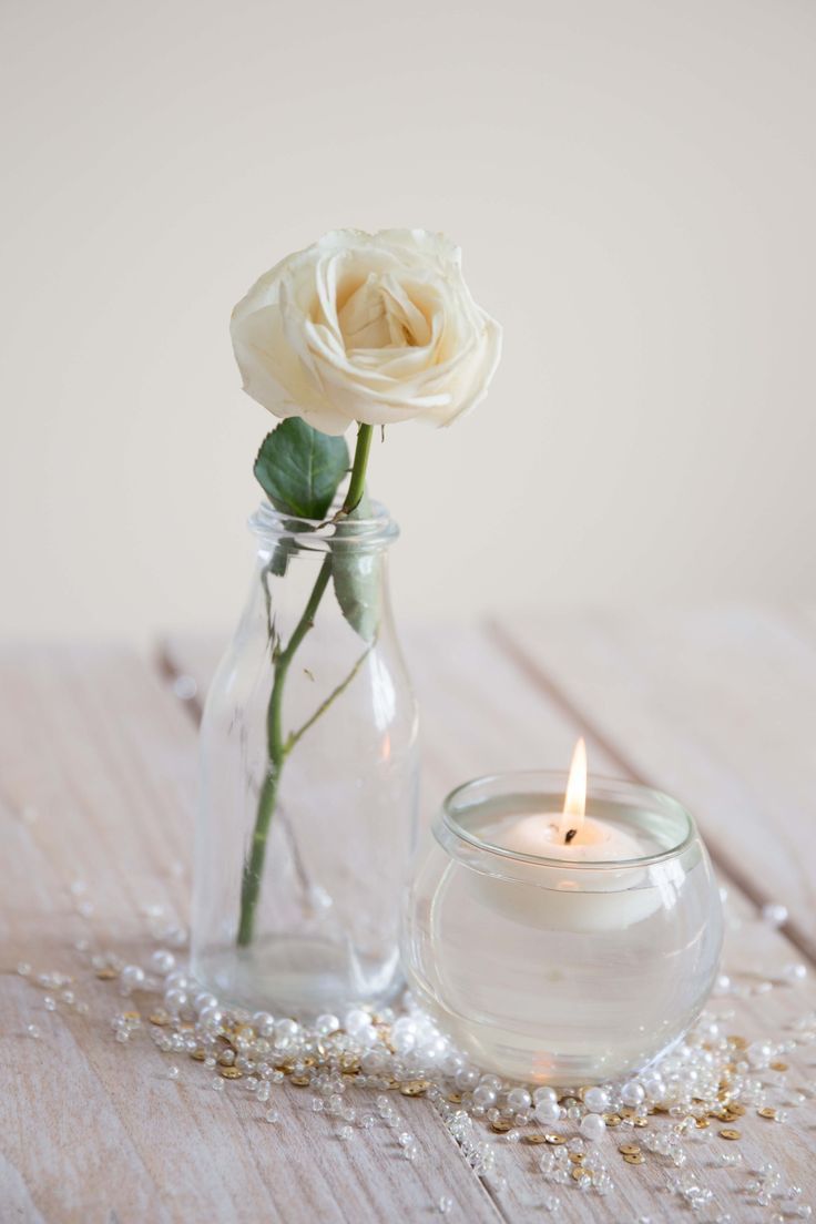 a single white rose in a glass jar next to a candle