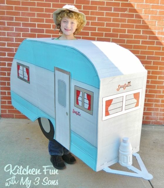 a young boy is standing next to a mailbox shaped like a child's camper