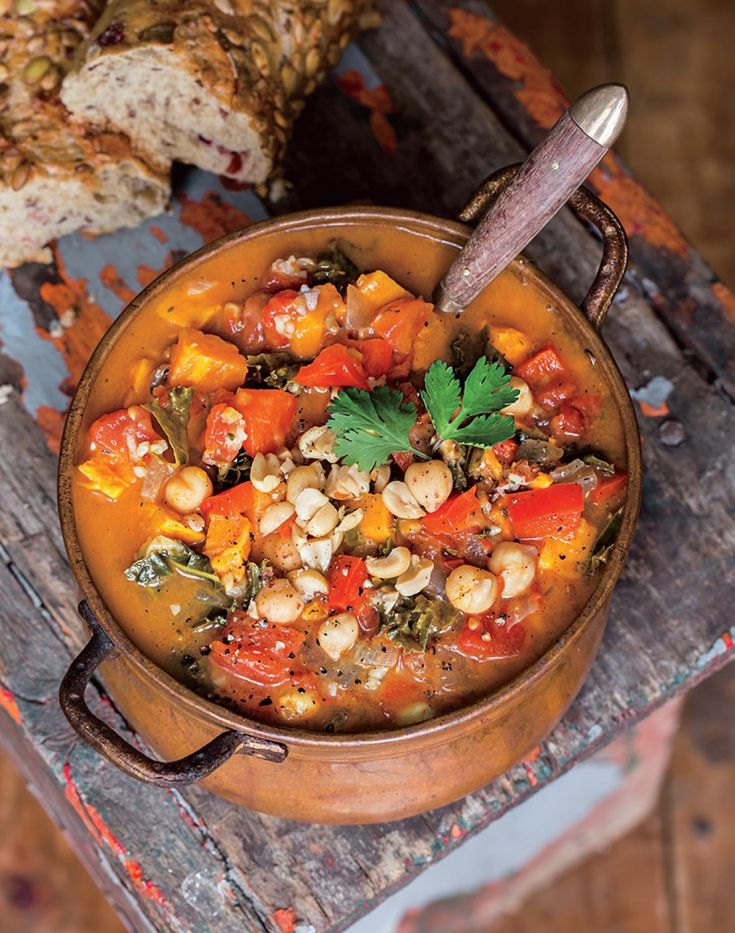 a bowl filled with food sitting on top of a wooden table next to some bread