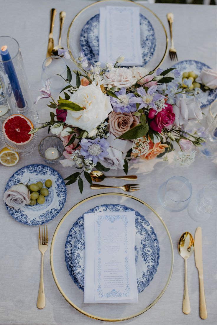 the table is set with blue and white plates, silverware, napkins, and flowers