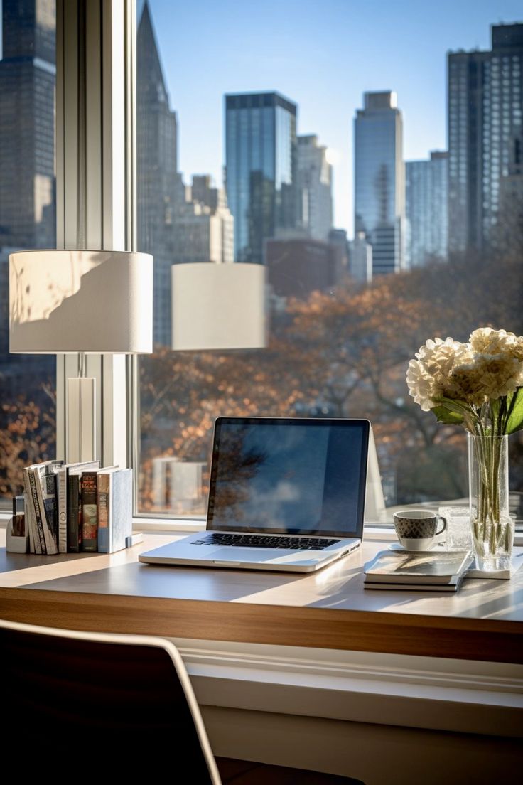 a laptop computer sitting on top of a desk next to a vase with flowers in it