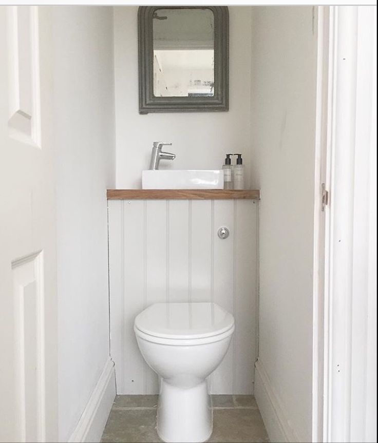 a white toilet sitting under a bathroom mirror next to a wooden shelf with a sink