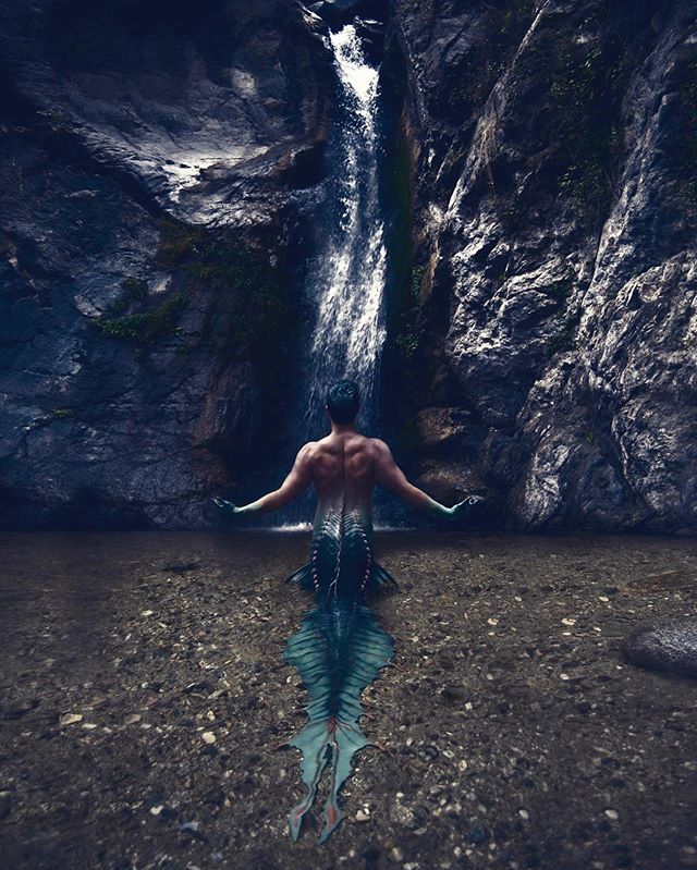 a man is swimming in the water near a waterfall