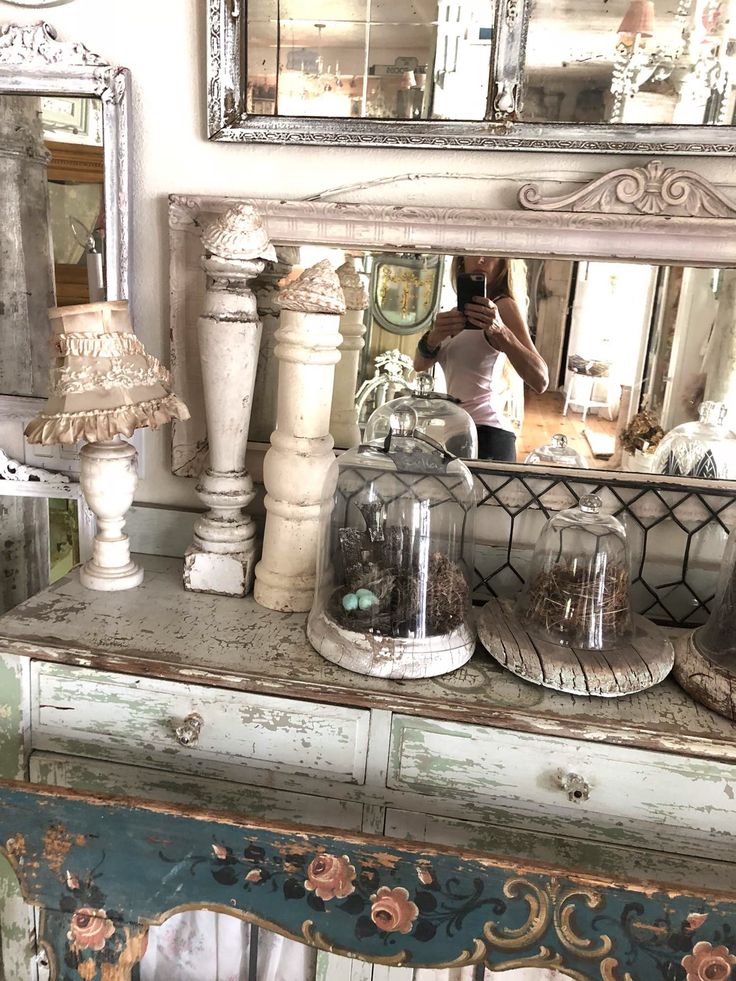 an old dresser with some glass jars on it and a person taking a photo in the mirror