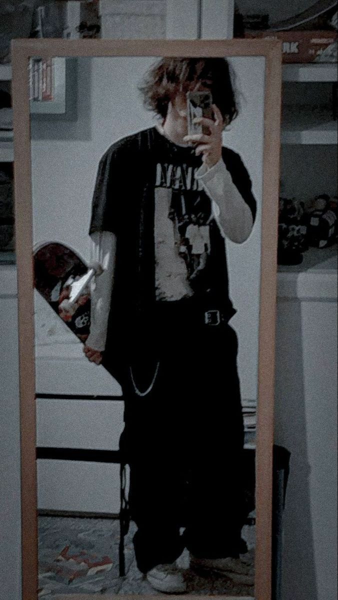 a young man taking a selfie in front of a mirror with his skateboard