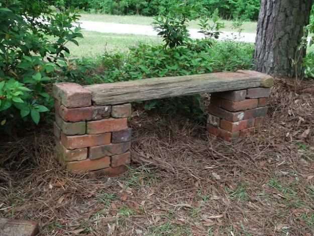 a bench made out of bricks sitting in the grass next to a tree and bushes