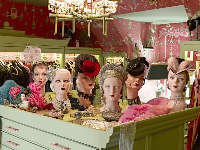 several mannequin heads are on display in a clothing store with pink and green wallpaper