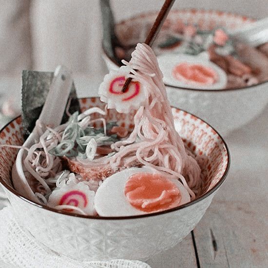 two bowls filled with noodles and meat on top of a white table next to utensils