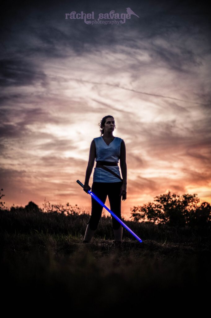 a woman holding two blue lightsabes in her hands while standing on top of a hill