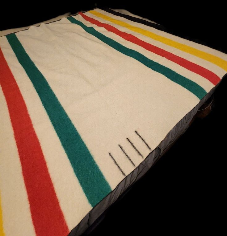 a multicolored striped blanket laying on top of a black surface with pins sticking out of it