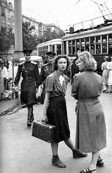 black and white photograph of two women walking down the street in front of a train