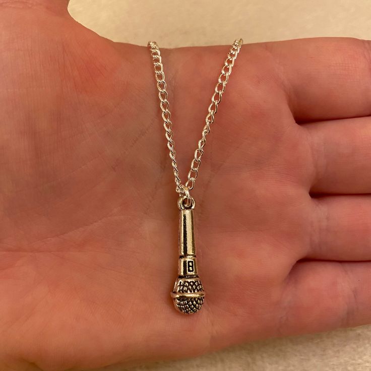 a person's hand is holding a silver necklace with a small metal object on it