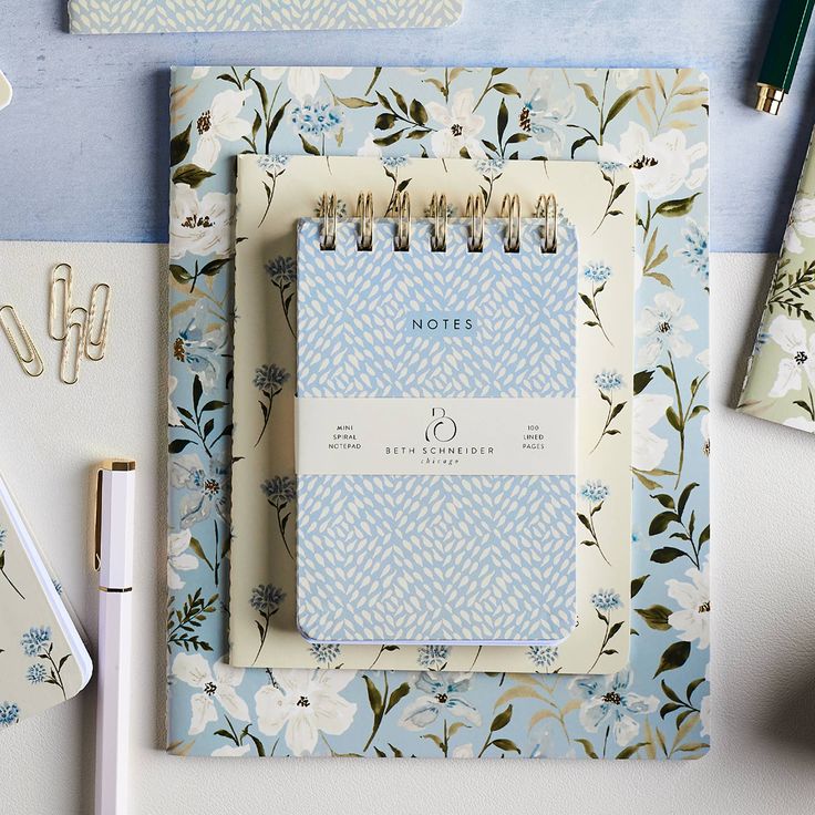 an open notebook on top of a blue and white flowered paper with gold pen