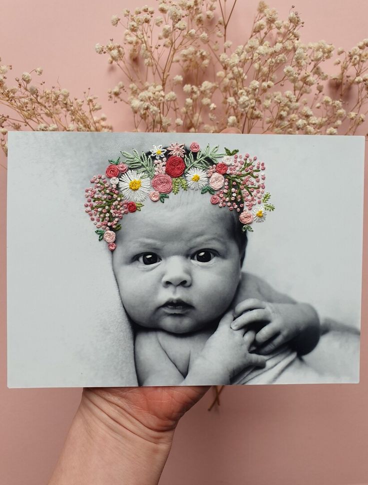 a hand holding up a card with an image of a baby wearing a flower crown