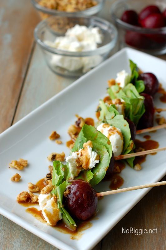 a white plate topped with meat and veggies on skewers next to bowls of cherries