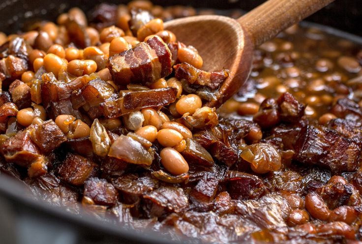 beans and bacon cooking in a pot with a wooden spoon on the side, ready to be eaten