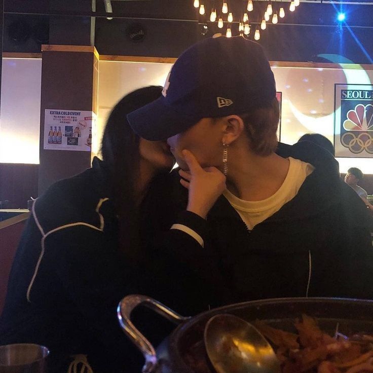 two people sitting at a table with food in front of them and one person kissing the other