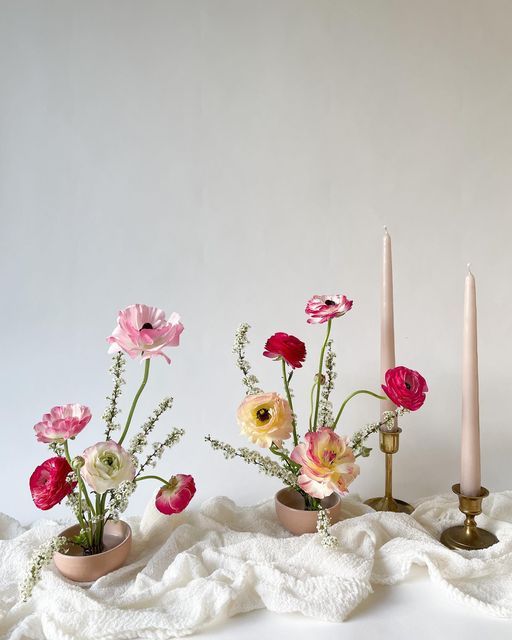 three small vases with flowers and candles on a white cloth next to each other