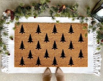 a person standing in front of a door mat with trees on it and pine cones