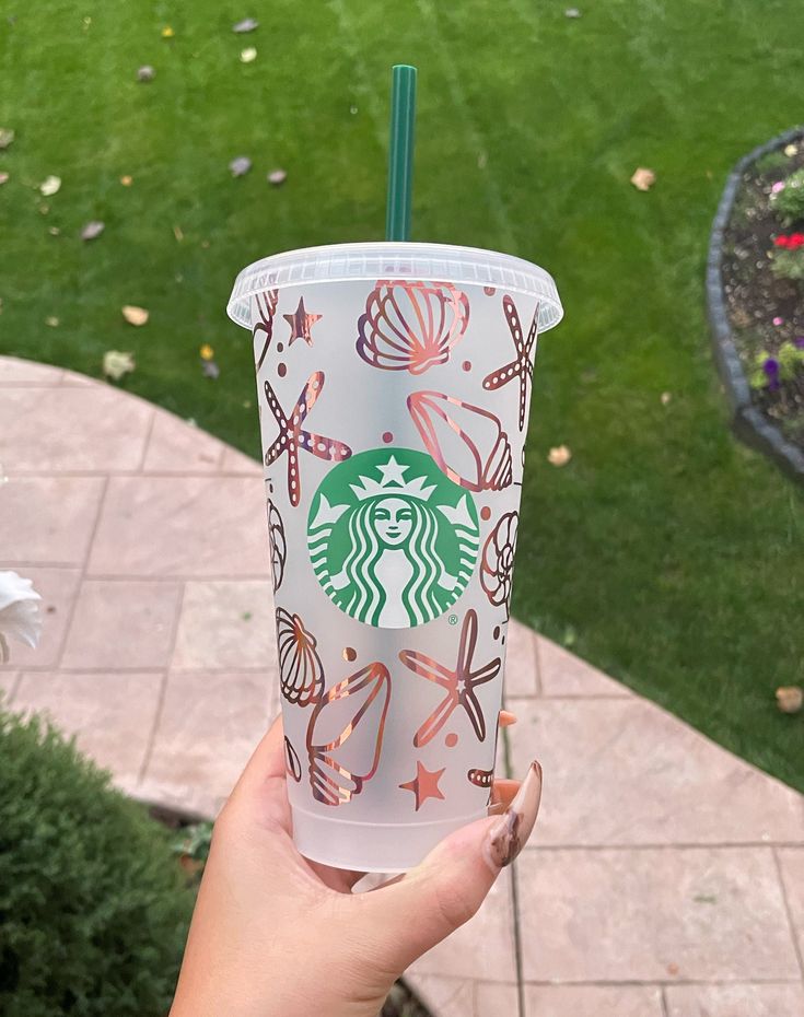 a hand holding up a starbucks cup in front of a brick walkway and grass area