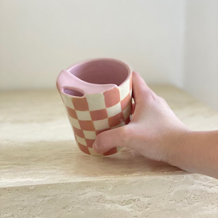 a hand holding a pink and white checkered cup