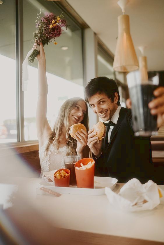 a man and woman sitting at a table with food in front of them holding up their hands